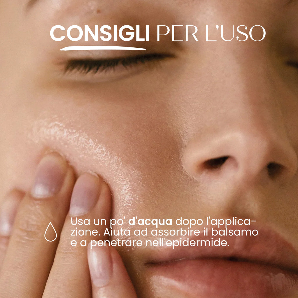 Primo piano di una mano che massaggia delicatamente un balsamo illuminante sulla guancia. Il testo spiega di usare un po' d'acqua dopo l'applicazione per favorire l'assorbimento e la penetrazione del prodotto nell'epidermide.