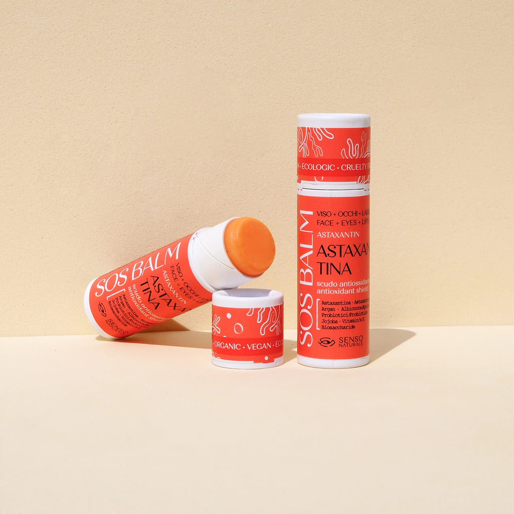 SOS Balm Senso Naturale con Astaxantina, balsamo stick arancione per viso, contorno occhi e labbra. La confezione eco-friendly mostra le scritte "Organic", "Vegan" e "Cruelty Free". Trattamento antiossidante e protettivo contro vento e freddo su sfondo neutro.